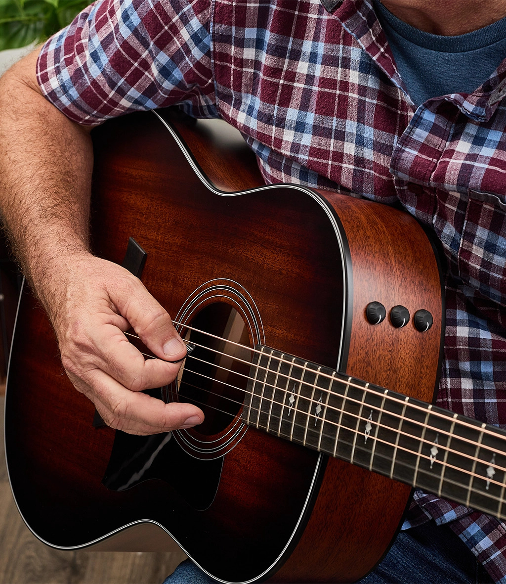 Close up shot of man wearing plaid shirt finger picking guitar