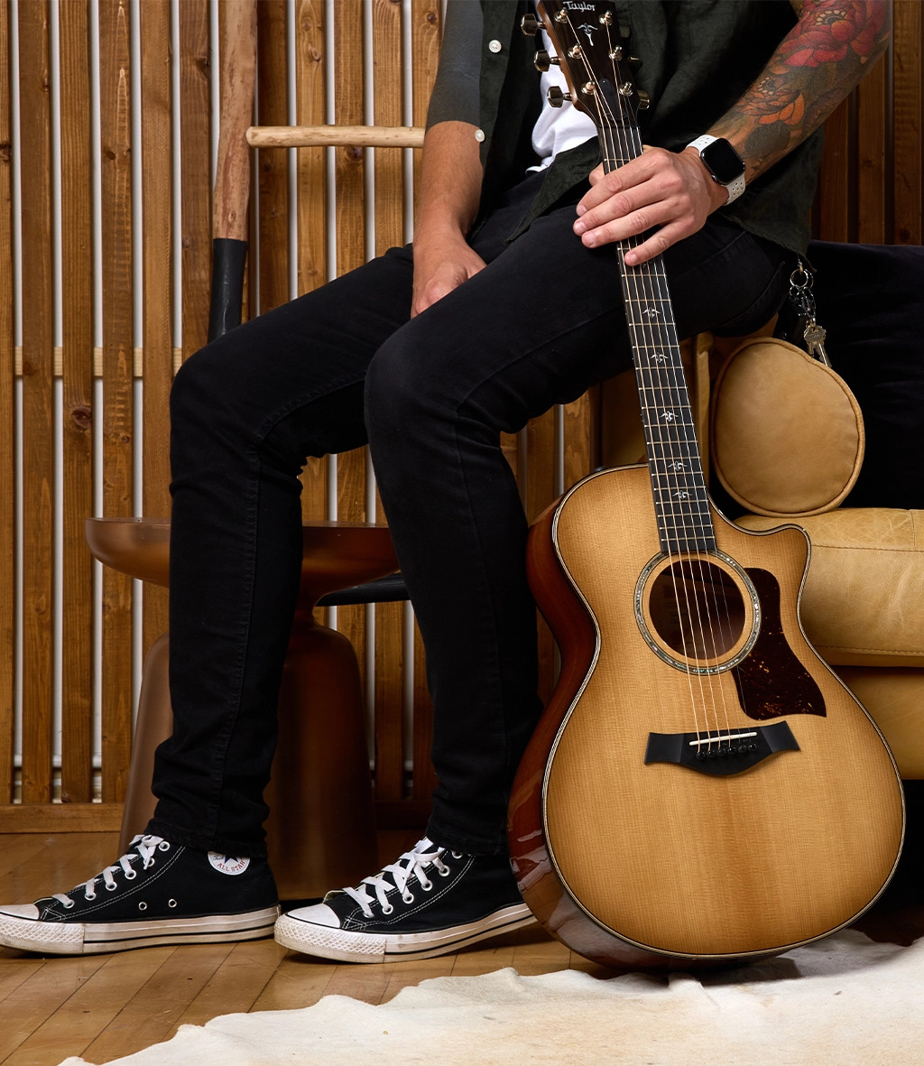 Man sitting on couch holding guitar upright