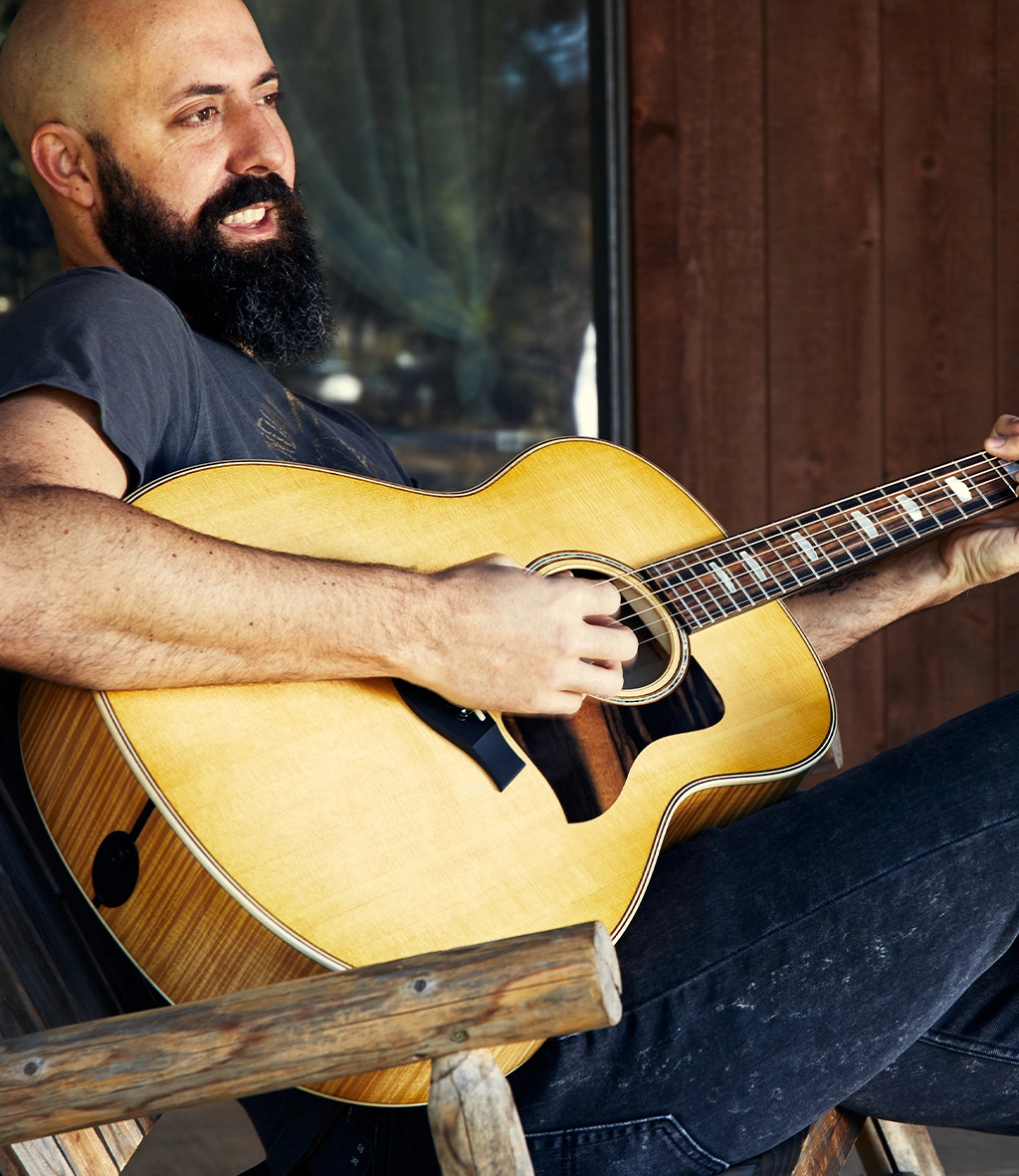 Man smiling while sitting down playing guitar