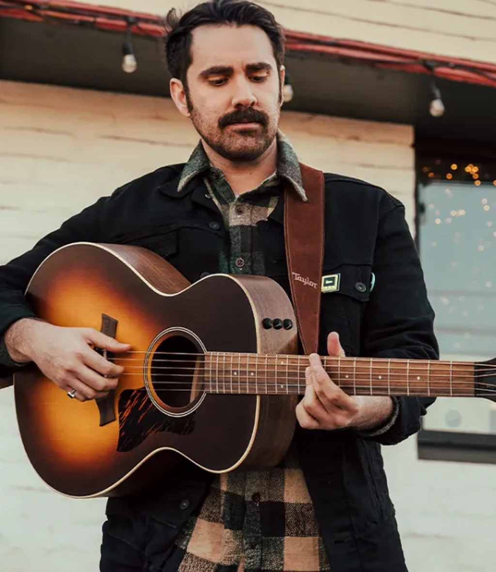 Man in dark clothing plays guitar standing up