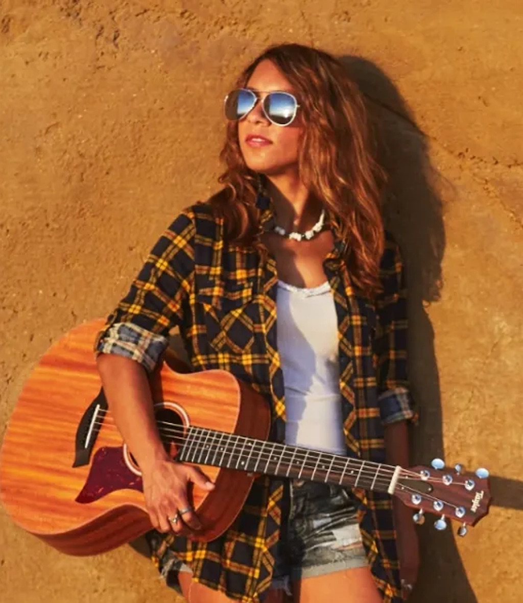 Girl leaning on wall wearing sunglasses plays the gs mini guitar