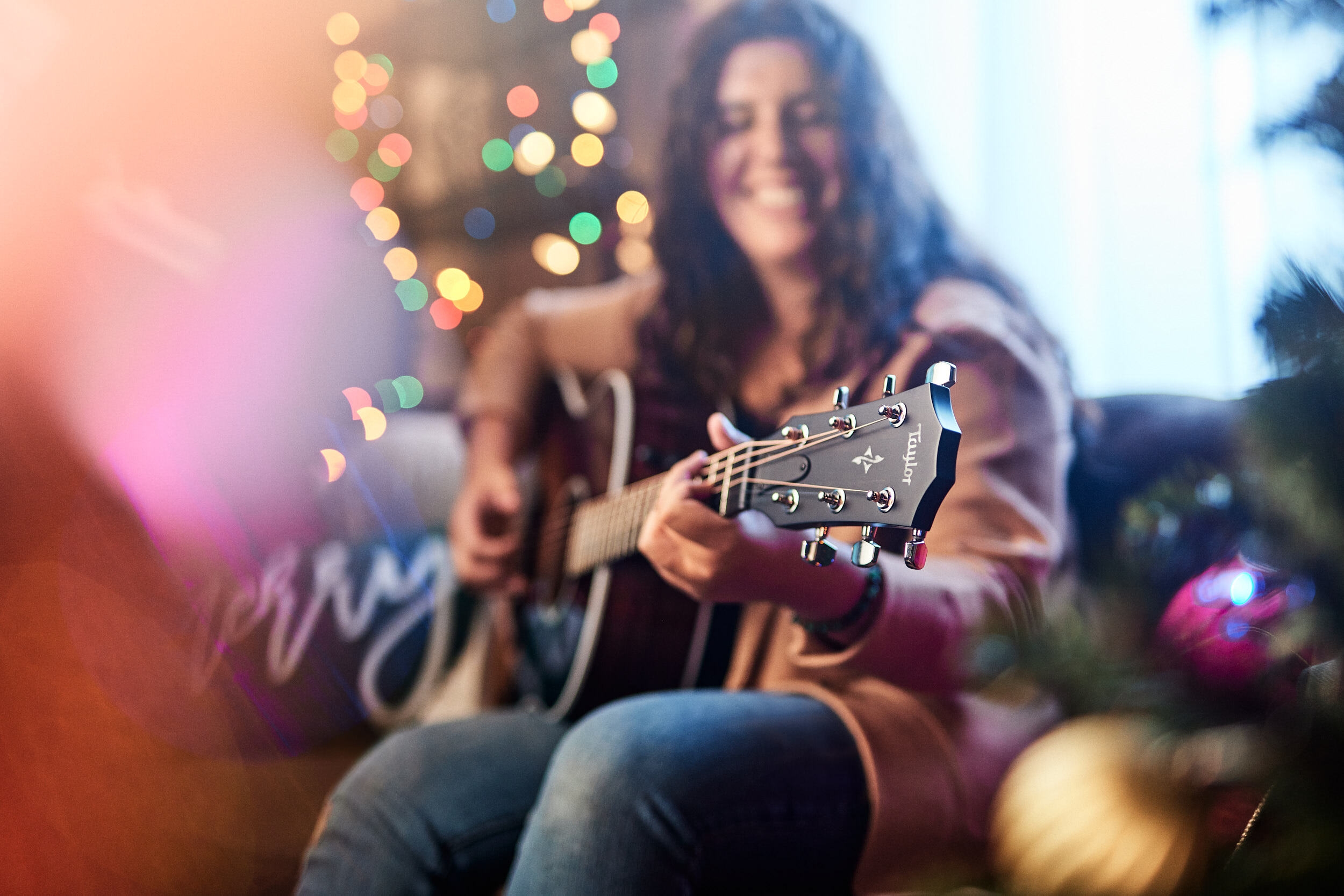 Girl playing guitar in front of christmas tree lit up