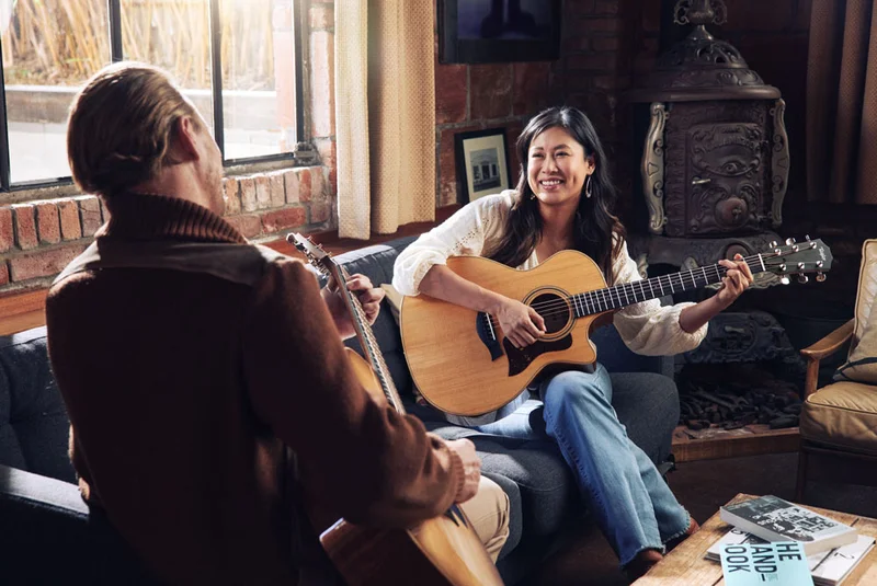 Woman and man laughing playing guitar on couch